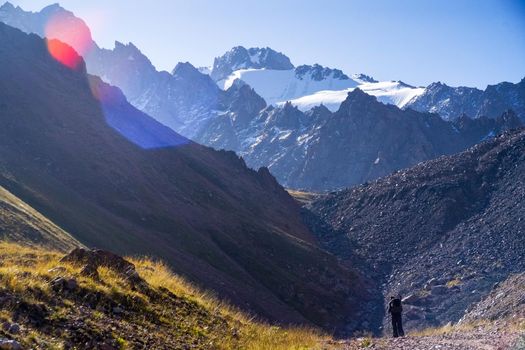 High mountains with snowy peaks in the national park in the sunshine, the traveler goes through a difficult route, is engaged in hiking and mountaineering.