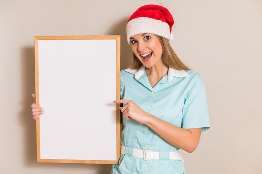 Portrait of nurse with Santa hat pointing at white board.