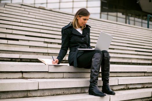 Beautiful businesswoman sitting on the staircase in the city and working.