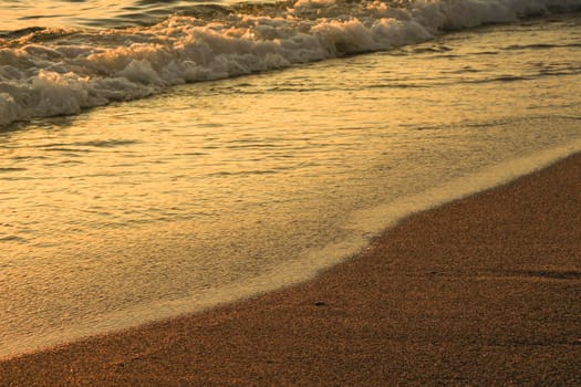 Colorful Waves and sand texture on the beach at sunset