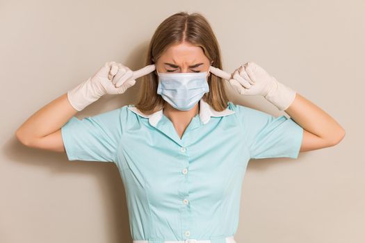 Portrait of overworked nurse with hands in ears.