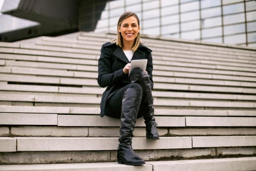 Beautiful businesswoman sitting on the staircase in the city and using digital tablet.