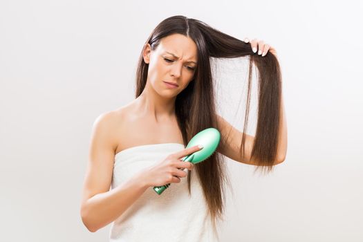 Image of angry woman brushing her hair on gray background.