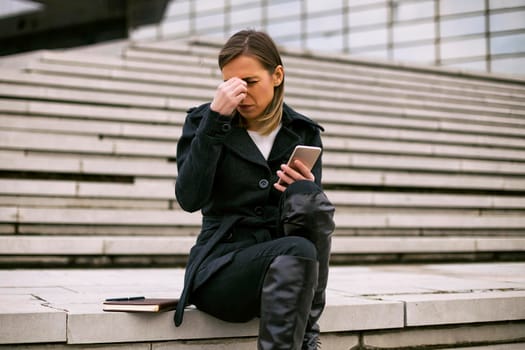 Businesswoman having headache and using phone while working outdoor.
