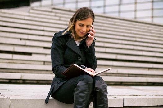 Businesswoman using phone and personal organizer while working outdoor.