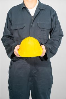 Worker standing in blue coverall holding yellow hardhat isolated on gray background