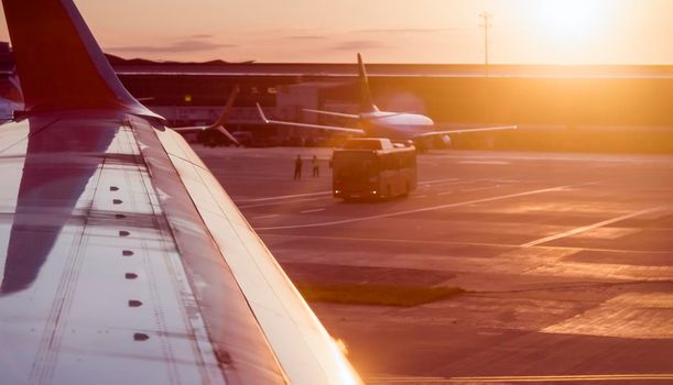 View from the plane window of the wing and other airplanes on the runway at sunset, travel and fly to the journey.