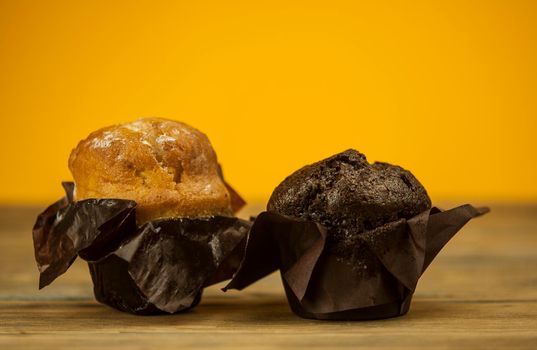 Homemade chocolate and vanilla cupcakes on a wooden table, sprinkled with powdered sugar