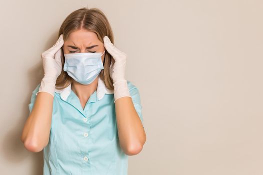 Tired nurse with with protective mask and gloves having headache.