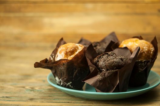 Homemade chocolate and vanilla cupcakes lie on ceramic plate on a wooden table, sprinkled with powdered sugar. Breakfast