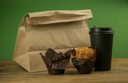 Homemade chocolate and vanilla cupcakes with paper disposable coffee cup on a wooden table, sprinkled with powdered sugar. Breakfast