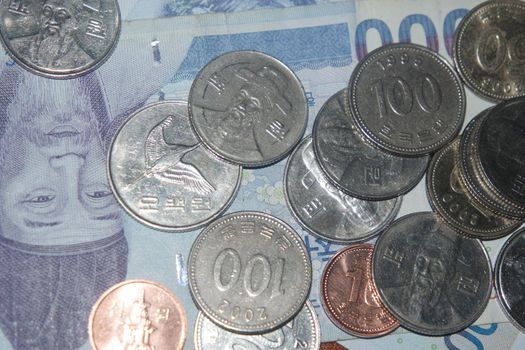 Silver shining Korean won coin scattered over Korean notes on a wooden floor.