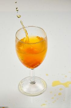 A dice falling into a glass of orange liquid caused a splash. Close up on white background