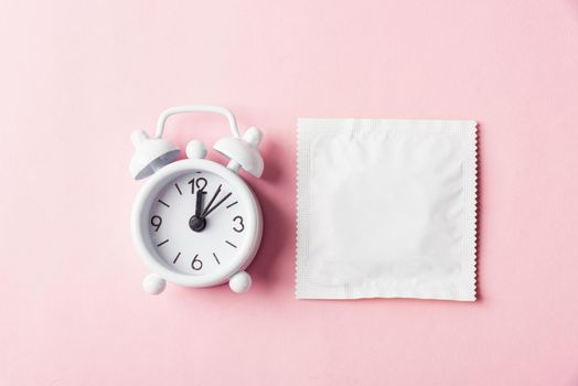 World sexual health or Aids day, condom in wrapper pack and Alarm clock birth control, studio shot isolated on a pink background, Safe sex and reproductive health concept