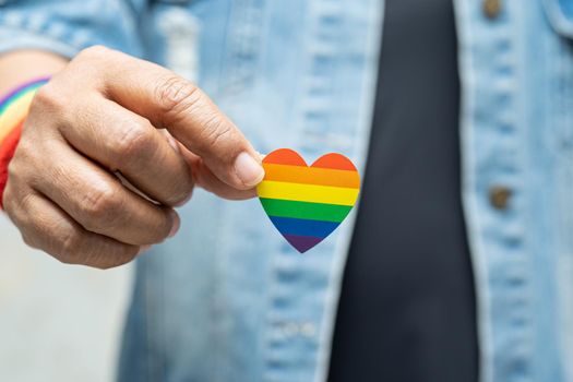 Asian lady wearing blue jean jacket or denim shirt and holding rainbow color flag heart, symbol of LGBT pride month celebrate annual in June social of gay, lesbian, bisexual, transgender, human rights.