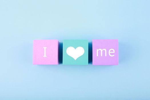Minimal trendy concept of mental health and self love and acceptance. I love me written on multicolored toy blocks in a row against bright blue background