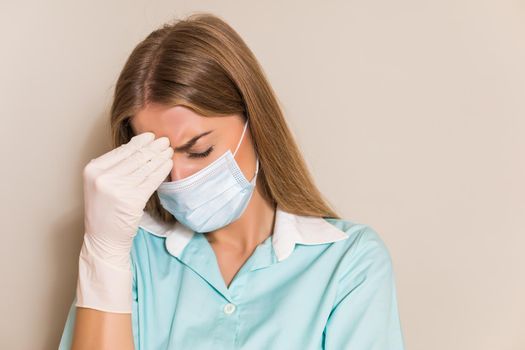 Tired nurse with with protective mask and gloves having headache.