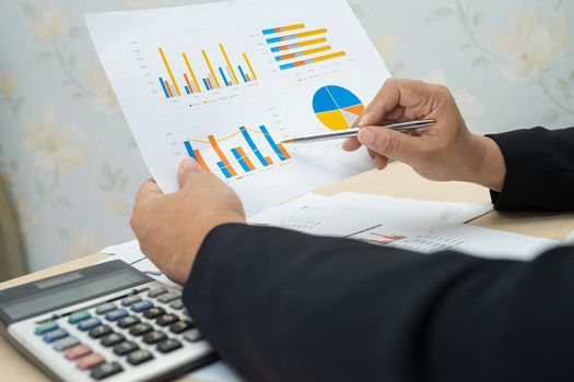 Asian accountant working and analyzing financial reports project accounting with chart graph and calculator in modern office, finance and business concept.