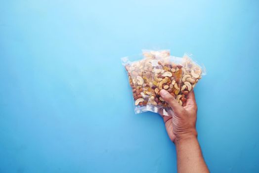 hand hold a packet of mixed nuts on blue background .