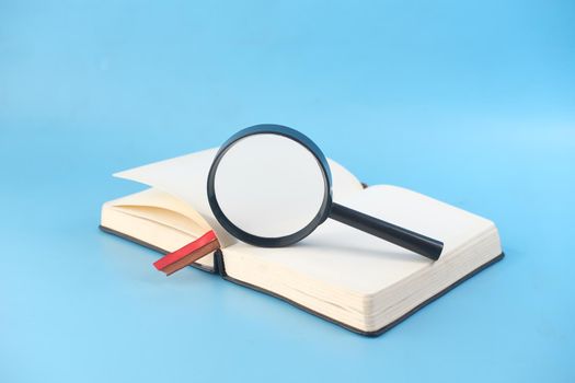 open book and magnifying glass on blue background