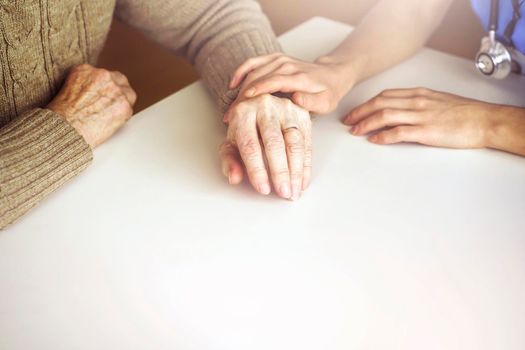 Young woman's hands hold grandmother's hands, an elderly patient. Handshake, caring, trust and support. Medicine, family and healthcare.