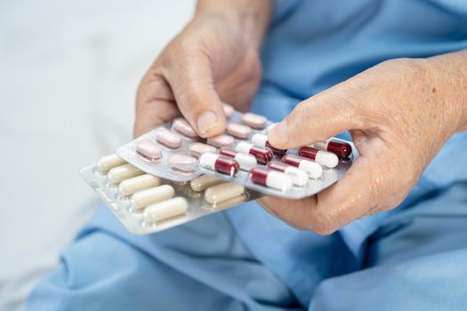 Asian senior or elderly old lady woman patient holding antibiotics capsule pills in blister packaging for treatment infection patient in hospital; Pharmacy drugstore concept.