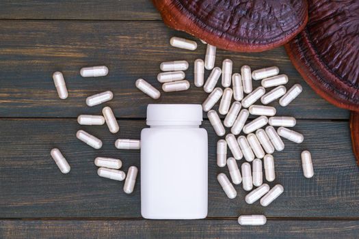 Close up of Ling zhi mushroom, Ganoderma lucidum mushroom and capsule with white bottle mockup on wooden floor