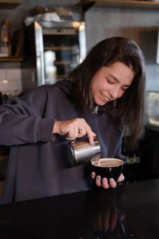 cute girl makes latte in coffee shop. Barista making coffee. Draws a drawing with milk on drink - cappuccino.