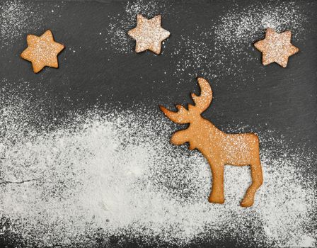 Close up gingerbread cookies with Christmas reindeer on black slate background with powdered white sugar icing and copy space, elevated top view, directly above