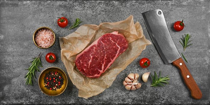 Close up one aged prime marbled raw sirloin beef steak on brown paper parchment wrapping, with cleaver knife and spices on stone table background, elevated top view, directly above