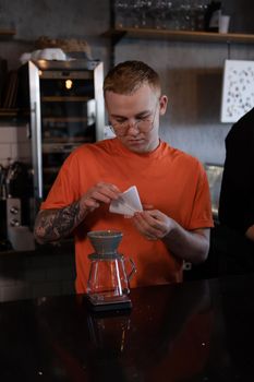 blonde guy in orange t-shirt preparing Alternative coffee brewing: chemex in modern loft coffee shop.