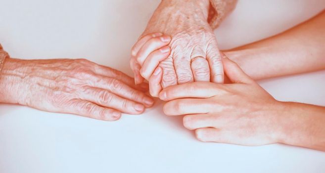 Young woman's hands hold grandmother's hands, an elderly patient. Handshake, caring, trust and support. Medicine, family and healthcare.