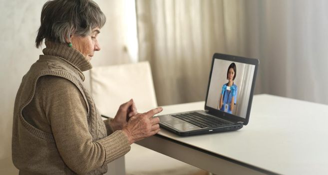 An elderly patient, retired person participates in a digital conversation with a nurse via a webcam. Aged woman talking using a video link with a female doctor, has an online consultation at home.
