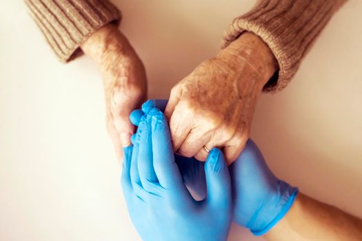 A doctor's hands in a blue gloves holds the hands of an elderly woman, a patient. Handshake, caring, trust and support. Medicine and healthcare.