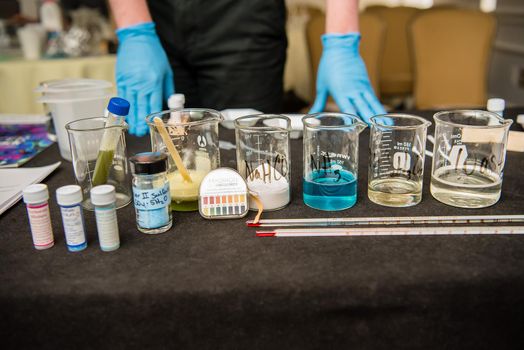 A close up of science experiment materials including colorful liquid filled beakers and various vials and stirring mechanisms.