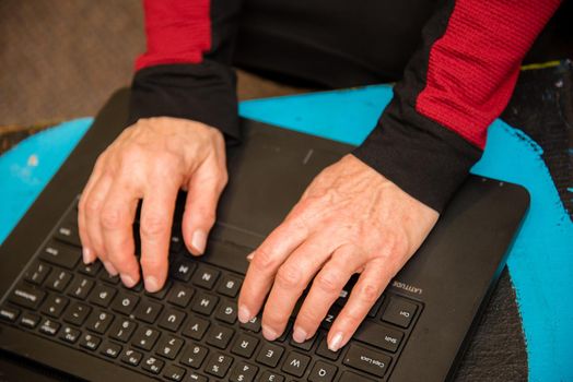 Overhead view of woman's hands typing on a black keyboard laptop.