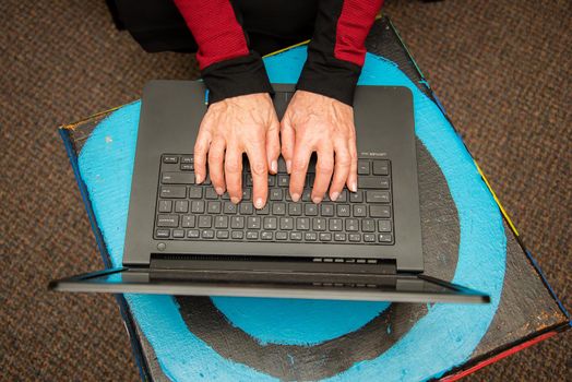 Overhead view of woman's hands typing on a black keyboard laptop.