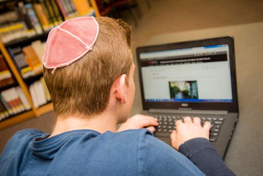 Young Jewish boy wearing yarmulke from the back sitting in a classroom setting with students.