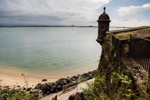 Scenic view of beach and castle tower in San Juan, Puerto Rico with clear waters and rocky beach.