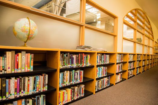 Colorful books in a school library with a globe sitting on the top shelf. Learning setting