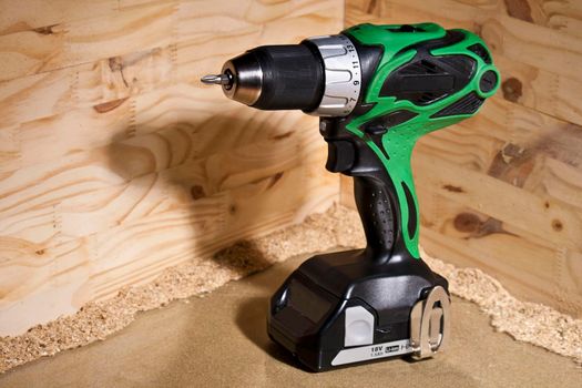 Conceptual photo of green power drill standing up on piece of wood with yellow construction color background vibrant industrial geometric building contractor