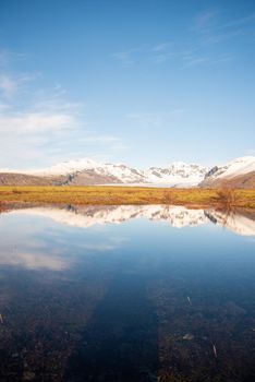 Icelandic mountain range with beautiful snowcapped mountains reflected into still water.