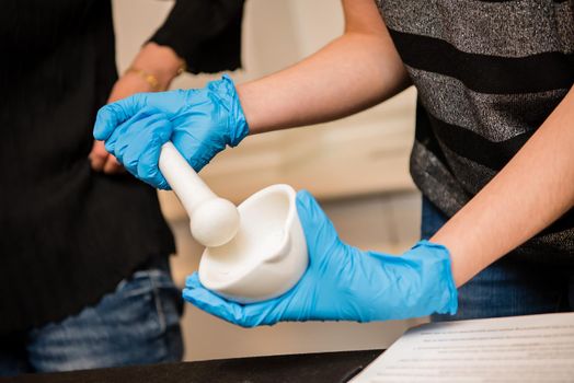 Close up of young hands wearing blue latex gloves using a mortar and pestle for a science experiment in a classroom lab.