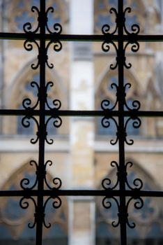 London, UK - February 4, 2017: Artistic view of gothic iron gate juxtaposed with cathedral windows blurred in background. Unique perspective