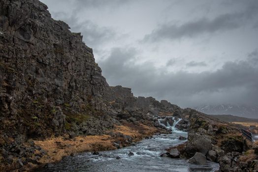 Dark rocky cliff with stormy skies and water rushing down a stream