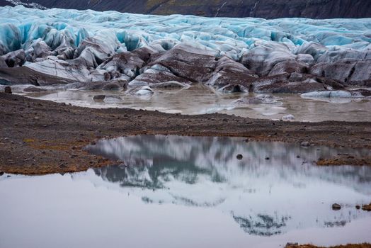 Magical view of bright blue Icelandic glacier with layers of glacier, volcanic ash, snow, and melted water with gorgeous reflection.