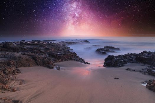 Milky way shimmers over the ocean water as it cascades over rocks in Reykjavik, Iceland.