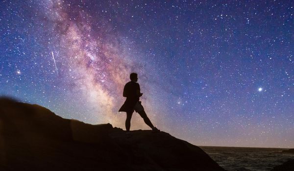 Night stars over woman’s silhouette at the ocean water as it cascades over rocks in Reykjavik, Iceland.