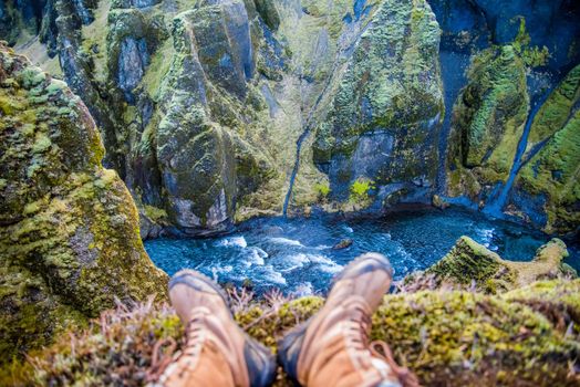 Fjaorargljufur, Iceland mossy green canyon with breathtaking views. View of hikers feet with boots on overlooking the river flowing through the canyon.