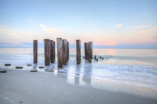 Sunrise over old pier on the ocean at Port Royal Beach in Naples, Florida.